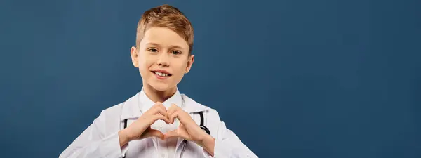 年轻的男孩穿着医生的衣服 双手插在蓝色的背景上 形成了一个心形 — 图库照片