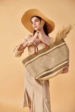 Young woman with long brunette hair striking a summer pose, radiating elegance in a straw hat while holding a bag. clipart