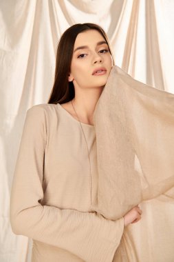 A young woman with long brunette hair strikes a pose in a beige top, exuding a serene summer mood in a studio setting. clipart