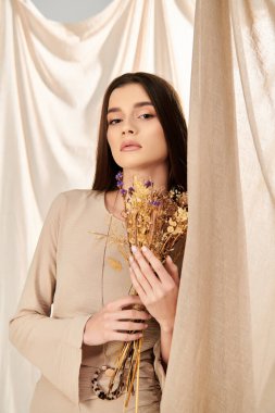 A young woman with long brunette hair holds a bunch of dried flowers, exuding a summery vibe in the studio. clipart