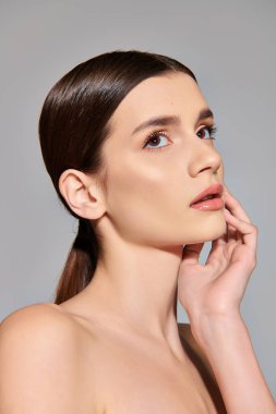 At kuyruklu esmer bir kadın, gri bir arkaplan karşısında duran stüdyoda zarif ve kendine güvenen bir poz veriyor..