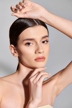 Esmer bir kadın, stüdyoda gri bir zemine nazikçe poz veriyor..