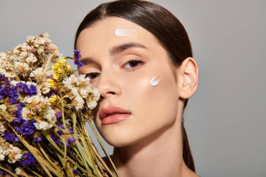 A young woman with brunette hair holds a bouquet of flowers while her face is painted white in a studio setting. clipart