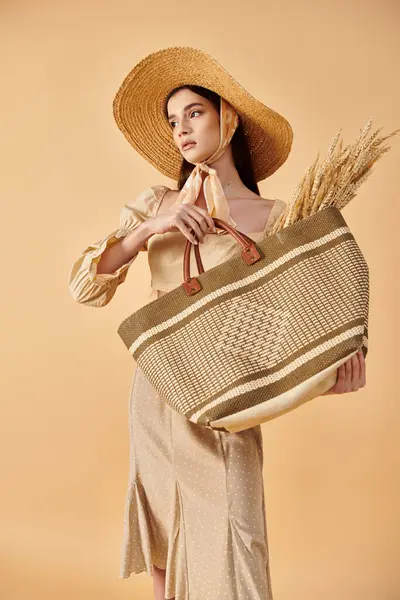 stock image Young woman with long brunette hair striking a summer pose, radiating elegance in a straw hat while holding a bag.