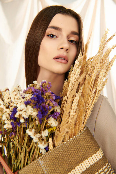A young woman with long brunette hair, exudes a summer vibe as she holds a bouquet of dried flowers in a studio setting.