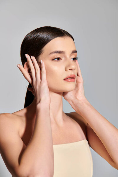 Молодая брюнетка нежно прикасается к лицу обеими руками, источая женскую красоту и самосознание..