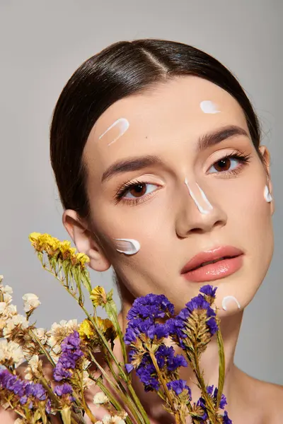 stock image A young brunette woman holds a bouquet of flowers while her face is covered in a luxurious cream, exuding natures beauty.