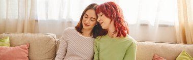 Genç ve mutlu lgbt çifti el ele tutuşup kanepede oturuyor.