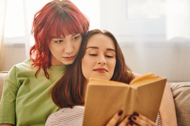 Rahatlamış lezbiyen çift birlikte okudukları sessiz anın tadını çıkarıyorlar, sevgi ve rahatlıkla sarılıyorlar.