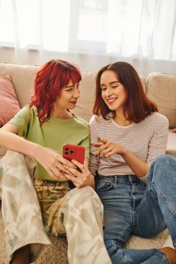 Mutlu genç lezbiyen çift gülümsüyor ve akıllı telefonu birlikte kullanıyorlar, modern yaşam tarzı ve bağlantı.