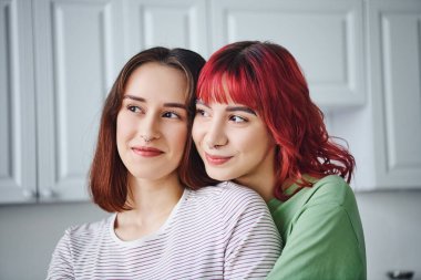 Kız arkadaşının omzuna yaslanmış kızıl saçlı neşeli ve piercingli lezbiyen kadın portresi.