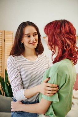 portrait of young and happy lesbian woman looking and embracing her female partner with red hair clipart