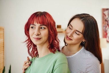 Genç ve neşeli lezbiyen kadının portresi. Evde kızıl saçlı bayan ortağına bakıyor.