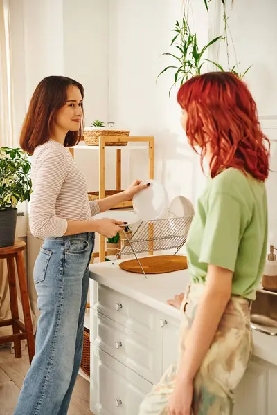 20代のレズビアンカップルは 居心地の良いキッチンの瞬間を楽しんで 愛と笑顔で料理を洗う — ストック写真