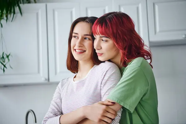 stock image portrait of joyful and pierced lesbian woman with red hair embracing her girlfriend at home