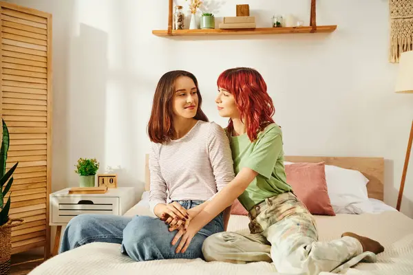 stock image Young lesbian couple in casual attire sharing a cozy moment in sunny bedroom, women in 20s