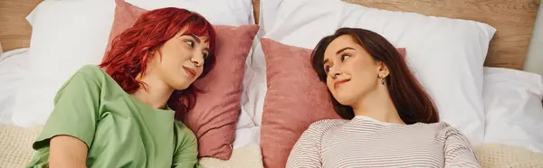 stock image horizontal banner of happy young lesbian couple looking at each other and lying together on bed