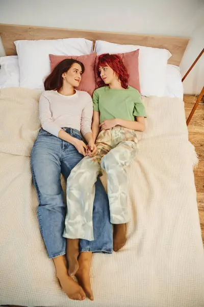幸せなレズビアンカップルのトップビューは ベッドで一緒に横たわり お互いを見ながら手を握っています — ストック写真