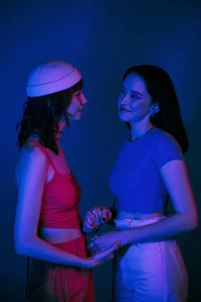 stock image happy lgbt couple in 20s, with bold makeup and stylish attire holding hands under purple lights