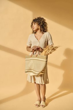 Güzel, kıvırcık saçlı, genç, Afro-Amerikan bir kadın. Stüdyoda altın buğdayla dolu bir sepet tutuyor..
