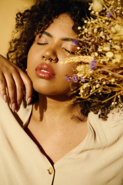 Kıvırcık saçlı, güzel bir Afrikalı Amerikalı kadın stüdyo ortamında canlı çiçekler tutuyor..