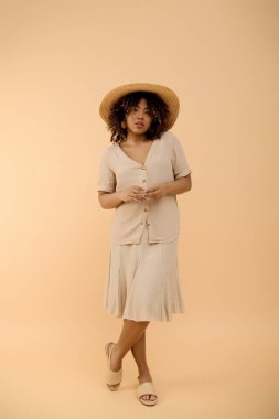 A beautiful young African American woman with curly hair elegantly posing in a floral summer dress and a stylish wide-brimmed hat. clipart