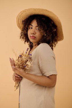 Güzel, kıvırcık saçlı, saman şapkalı ve elinde bir buket çiçekle durgun bir anda bekleyen Afro-Amerikan bir kadın..