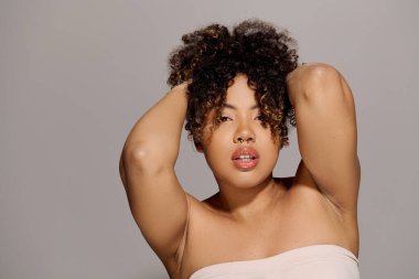Kıvırcık saçlı, güzel bir Afro-Amerikan kadın resim için stüdyoda zarifçe poz veriyor..