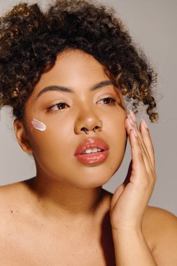 Güzel, kıvırcık saçlı, genç bir Afro-Amerikan kadın stüdyo ortamında yanağında dikkat çekici beyaz bir krem sergiliyor..