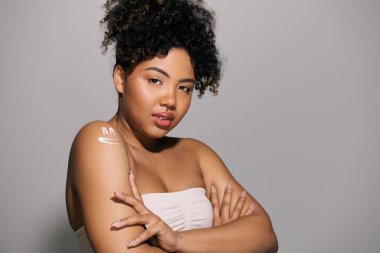 Kıvırcık saçlı Afrikalı bir kadın, stüdyoda duruyor, kollarını beyaz bir havluya sarmış..