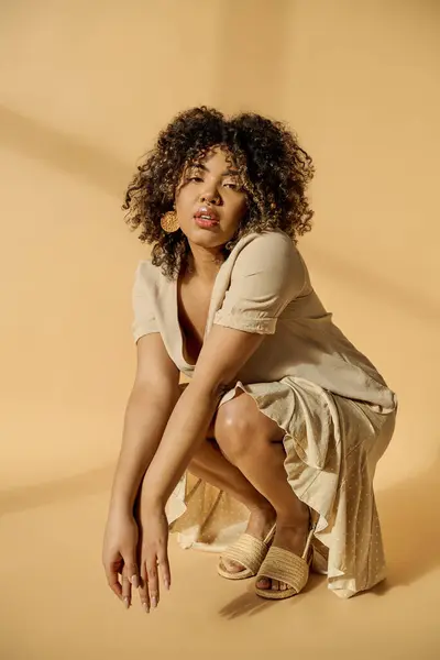 stock image A beautiful young African American woman with curly hair sits on the ground, striking a pose for a portrait in a studio setting.