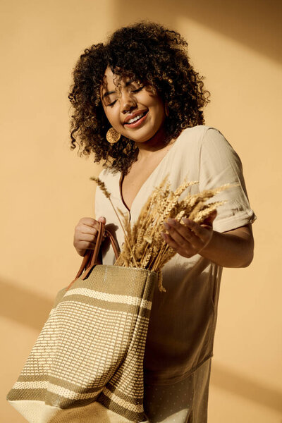 A beautiful young African American woman with curly hair holds a bag filled with wheat, embodying a connection to nature and abundance.