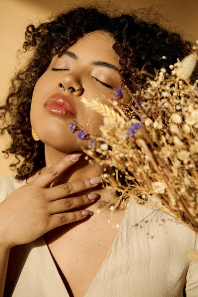 A beautiful young African American woman in a summer dress, holding a bunch of dried flowers with curly hair in a studio setting.