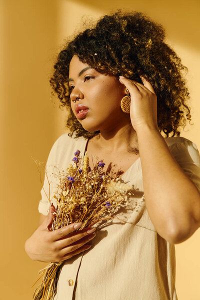 A beautiful African American woman with curly hair gracefully holding a bouquet of dried flowers.