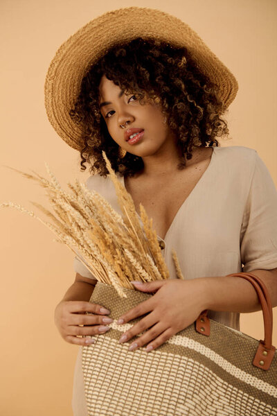Beautiful African American woman in a straw hat holding a stylish bag, exuding elegance and sophistication in a studio setting.