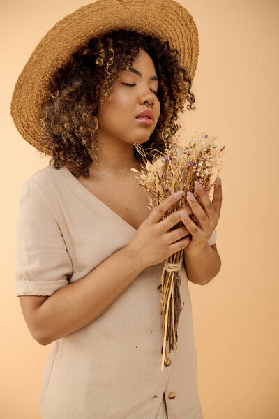 A captivating young African American woman with curly hair, wearing a straw hat, holding a bunch of dried flowers.