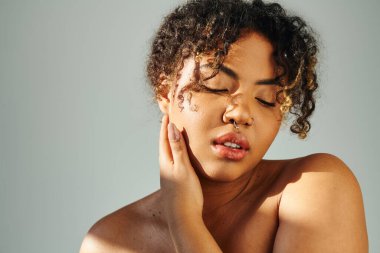 Afro-Amerikalı bir kadın zarif bir şekilde yüzünü eliyle kapatıyor..