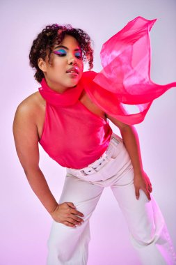 Beyaz pantolon ve pembe bluzla aktif poz veren şık bir Afro-Amerikan kadın..