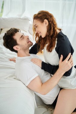 Bir erkek ve bir kadın bir yatakta huzur içinde uzanıyorlar, sıcak bir yatak odası ortamında birlikte hassas bir anı paylaşıyorlar..