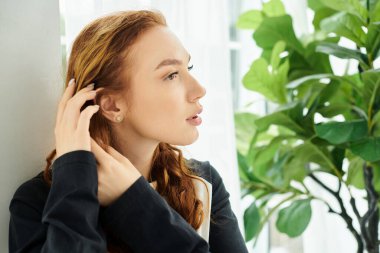 Huzurlu bir anda, sakin bir ortamda yemyeşil bir saksının yanındaki duvara yaslanmış bir kadın..