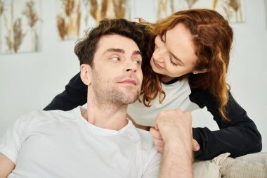 Bir erkek ve bir kadın rahat bir kanepede birlikte oturur, huzurlu ve samimi bir ortamda birbirlerine eşlik ederler..