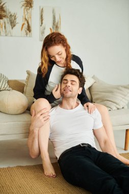 Bir erkek ve kadın birlikte oturur, güneşli bir yatak odasının sıcaklığında sessiz bir anı paylaşırlar..