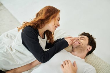 Bir erkek ve bir kadın, bir çift, yatağa uzanmış, rahat bir yatak odasında huzur ve yakınlık anlarını paylaşıyorlar..