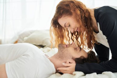 Bir erkek ve bir kadın bir yatakta yan yana uzanıyorlar, birbirlerine sevgi ve sükunetle eşlik ediyorlar..