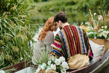 A man and woman dressed in boho style clothes drift in a boat adorned with flowers through a lush green park. clipart