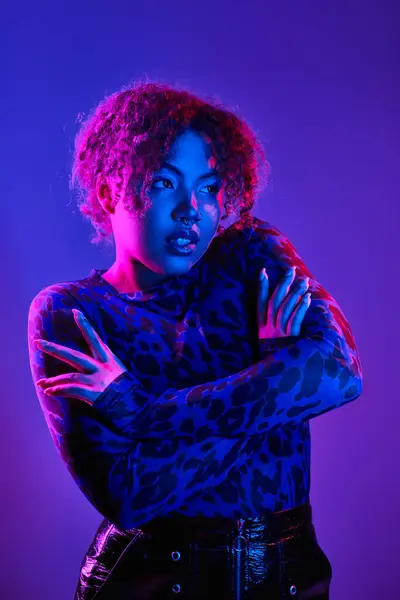 stock image African American woman stands confidently, arms crossed, against vivid purple background.