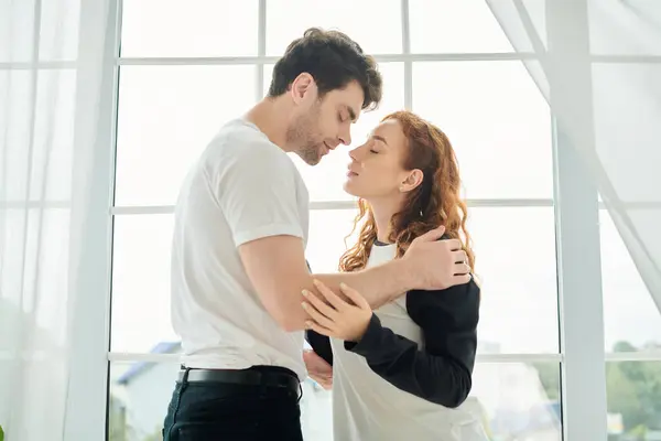 stock image A man and a woman stand peacefully side by side in front of a window, embracing a serene moment together.