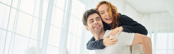 A man tenderly carries a woman in his arms in a bedroom setting, showcasing love and support.