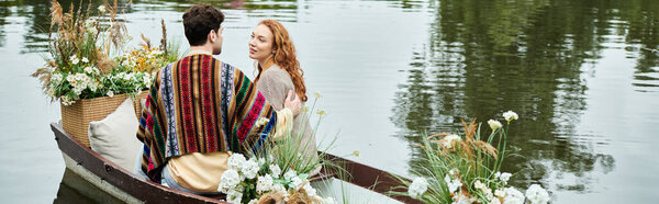 A couple in boho attire peacefully row a boat adorned with flowers in a lush green park.