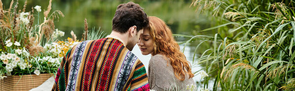 A man and a woman, dressed in boho style attire, snuggled up together under a cozy blanket in a lush green park.